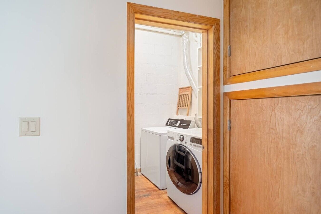 Lavandería con lavadora y secadora, marco de puerta de madera y pared de ladrillo blanco.