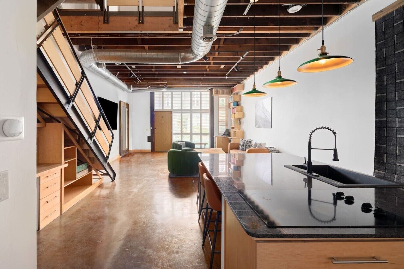 Een moderne keuken met een zwart aanrecht, een roestvrijstalen spoelbak en groene hanglampen.