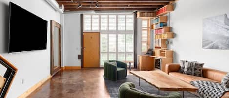 A modern living space with a flat-screen TV, a wooden table, a sofa, and a bookshelf.