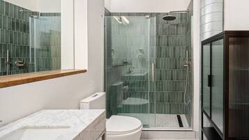 A modern bathroom with a glass-enclosed shower, a white toilet, and a marble sink.