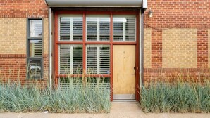 A brick building with a wooden door, large windows with blinds, and a small overhang above the door.