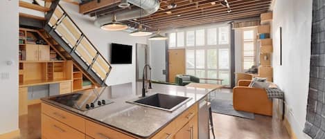 A modern kitchen with a central island, built-in cabinetry, and a staircase with a wooden finish.