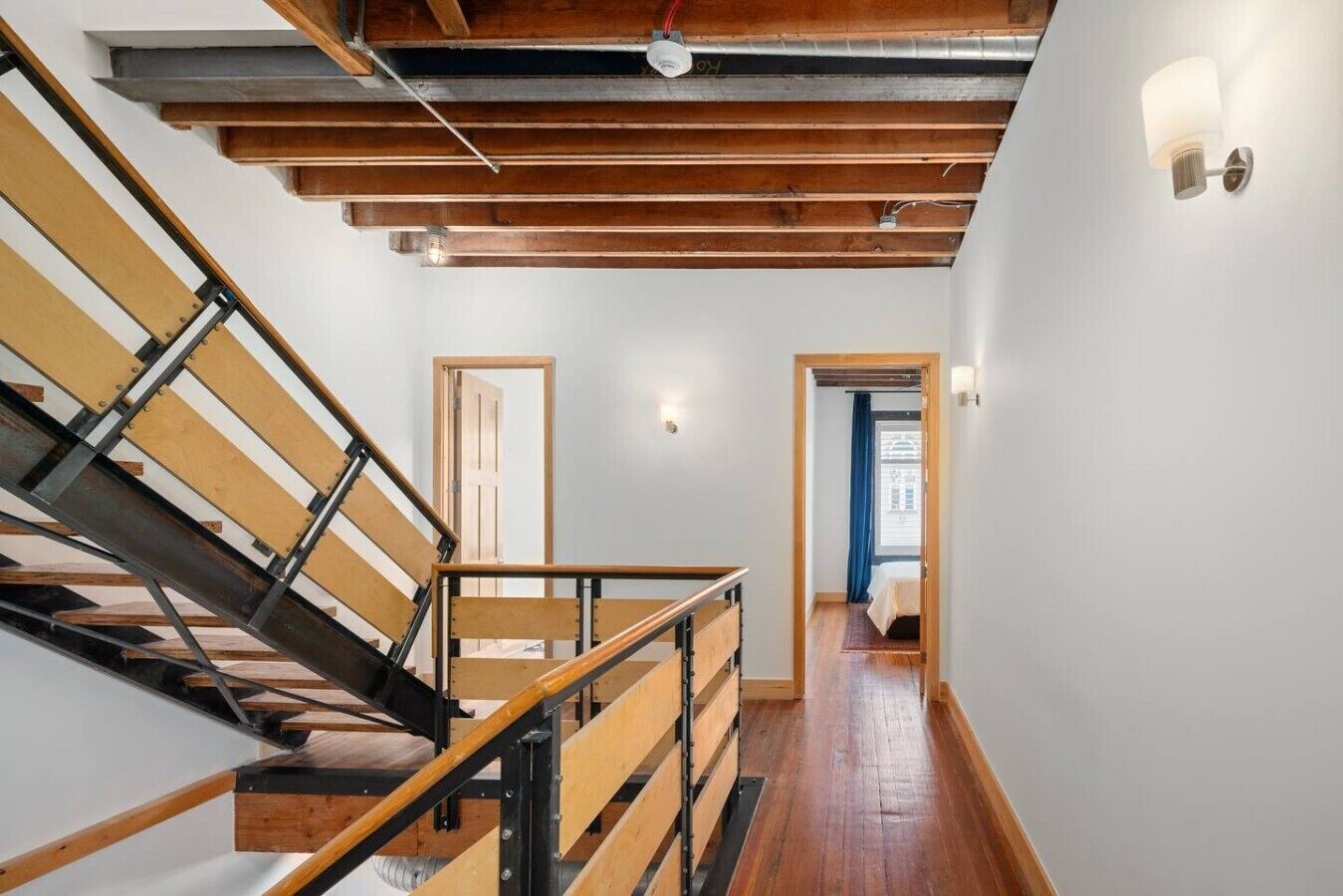 Een trap met houten treden en metalen leuningen die leidt naar een kamer met een bed en een raam.