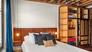 A hotel room with a large bed, a wooden headboard, a bookshelf, and a window with curtains.