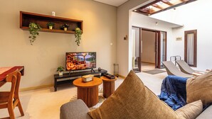 A modern living room with a flat-screen TV, wooden furniture, and a view of the outdoors.