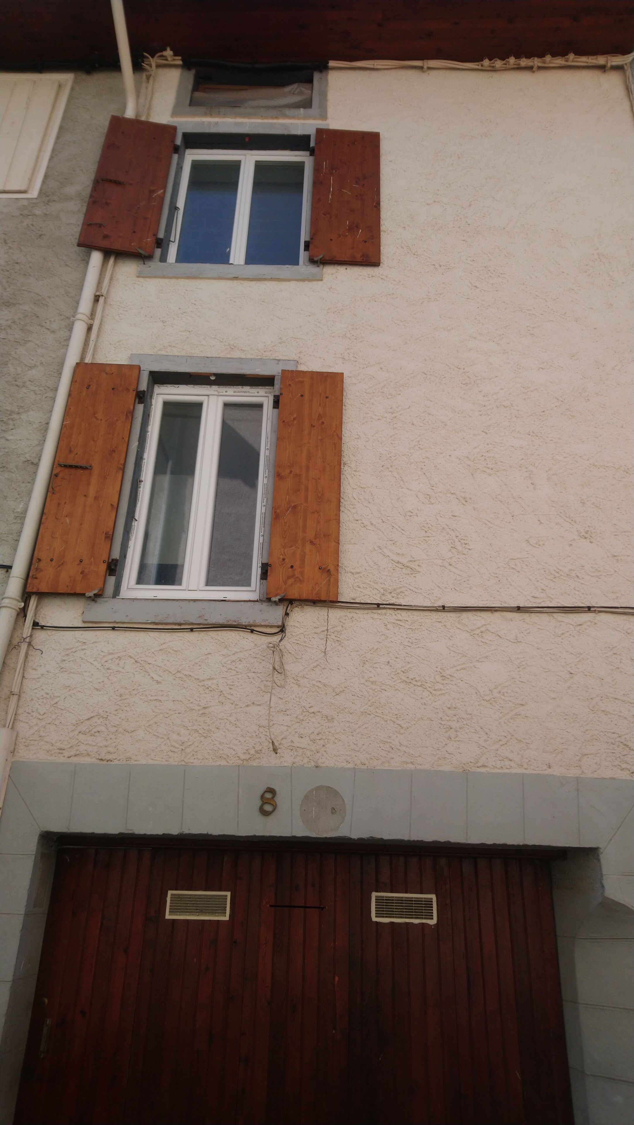A building with two windows, each with wooden shutters, and a garage door with a number plate.