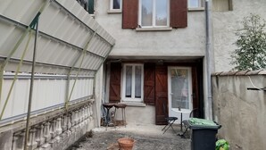 Et toetagers hus med en lille balkon, en dør med et vindue og et bord med en stol udenfor.
