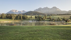 Vista para o lago com montanhas ao fundo, uma área gramada e um pequeno píer.