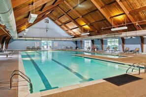 An indoor swimming pool with a high wooden ceiling, clear pool area, and lounge chairs.