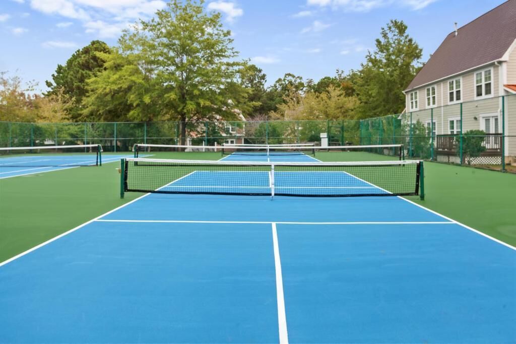 Een tennisbaan met net, omheind door een hek, en een gebouw op de achtergrond.
