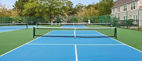 A tennis court with a net, surrounded by a fence, and a building in the background.