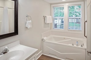 A bathroom with a white bathtub, a sink, a mirror, and a window with blinds.