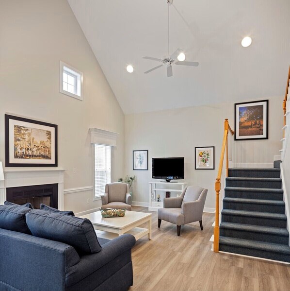 A spacious living room with a fireplace, a television, a staircase, and a ceiling fan.