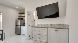 A modern kitchen with white cabinetry, a granite countertop, and a flat-screen TV mounted above the counter. - Poolside Studio on Padre (#2) (South Padre Island)