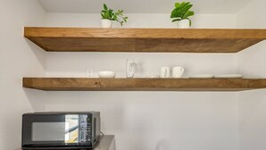 A kitchen with two wooden shelves, a microwave, and a small potted plant. - Poolside Studio on Padre (#2) (South Padre Island)