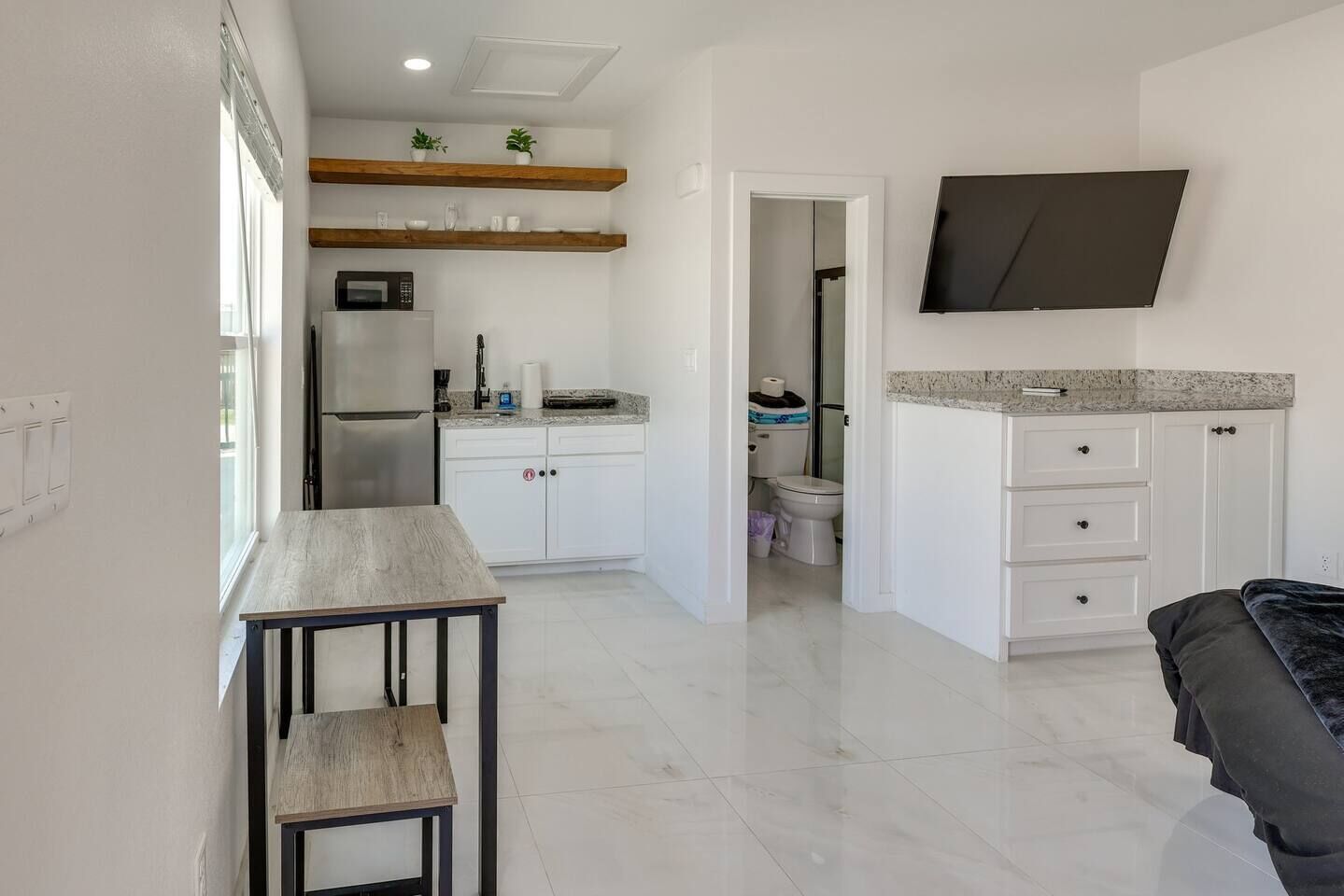Une cuisine moderne avec des meubles blancs, un four à micro-ondes et un four encastré. On y trouve également un coin repas avec une table et des chaises, ainsi qu’un téléviseur fixé au mur.