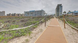 A sandy pathway leading to a beachfront hotel with multiple floors and balconies. - Poolside Studio on Padre (#2) (South Padre Island)