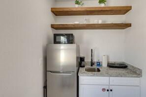 Una cocina con refrigerador de acero inoxidable, microondas, cafetera, lavamanos y encimera de granito.