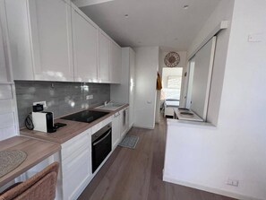 A modern kitchen with white cabinets, a black stove, and a window with a view. - Stintino - Anna Apartment - Residential Area (Stintino)
