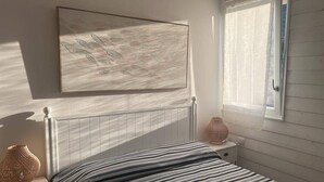 Ein Schlafzimmer mit Bett, Nachttisch, Lampe und einem Fenster mit Vorhängen.