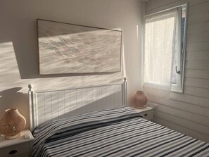 A bedroom with a bed, bedside table, lamp, and a window with curtains. - Stintino - Anna Apartment - Residential Area (Stintino)