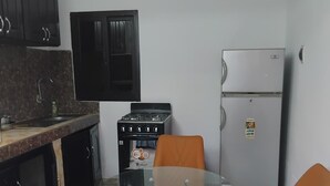 Uma cozinha compacta com fogão a gás, geladeira, mesa redonda de vidro e duas cadeiras.