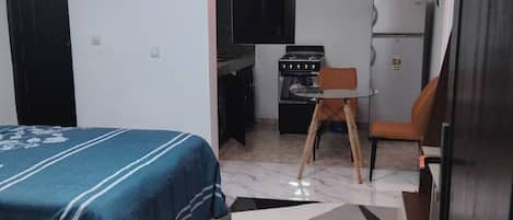 Een kleine kamer met een bed, een kitchenette en een eethoek.