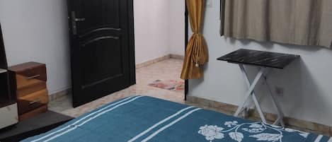 A bedroom with a bed, a door, a curtain, a small table, and a hanging light fixture.