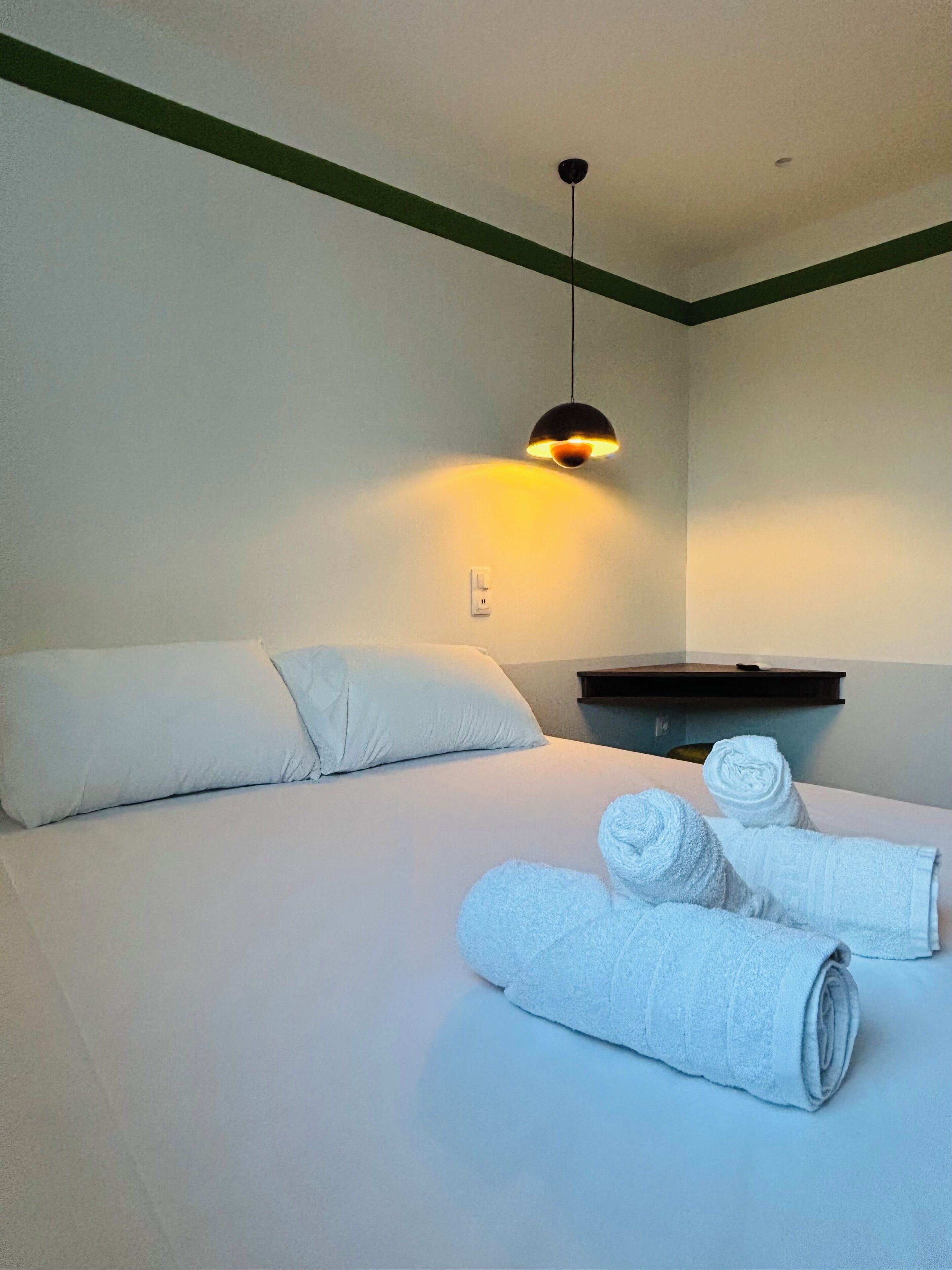 Habitación de hotel con cama, almohadas, mesita de noche y toallas dobladas.