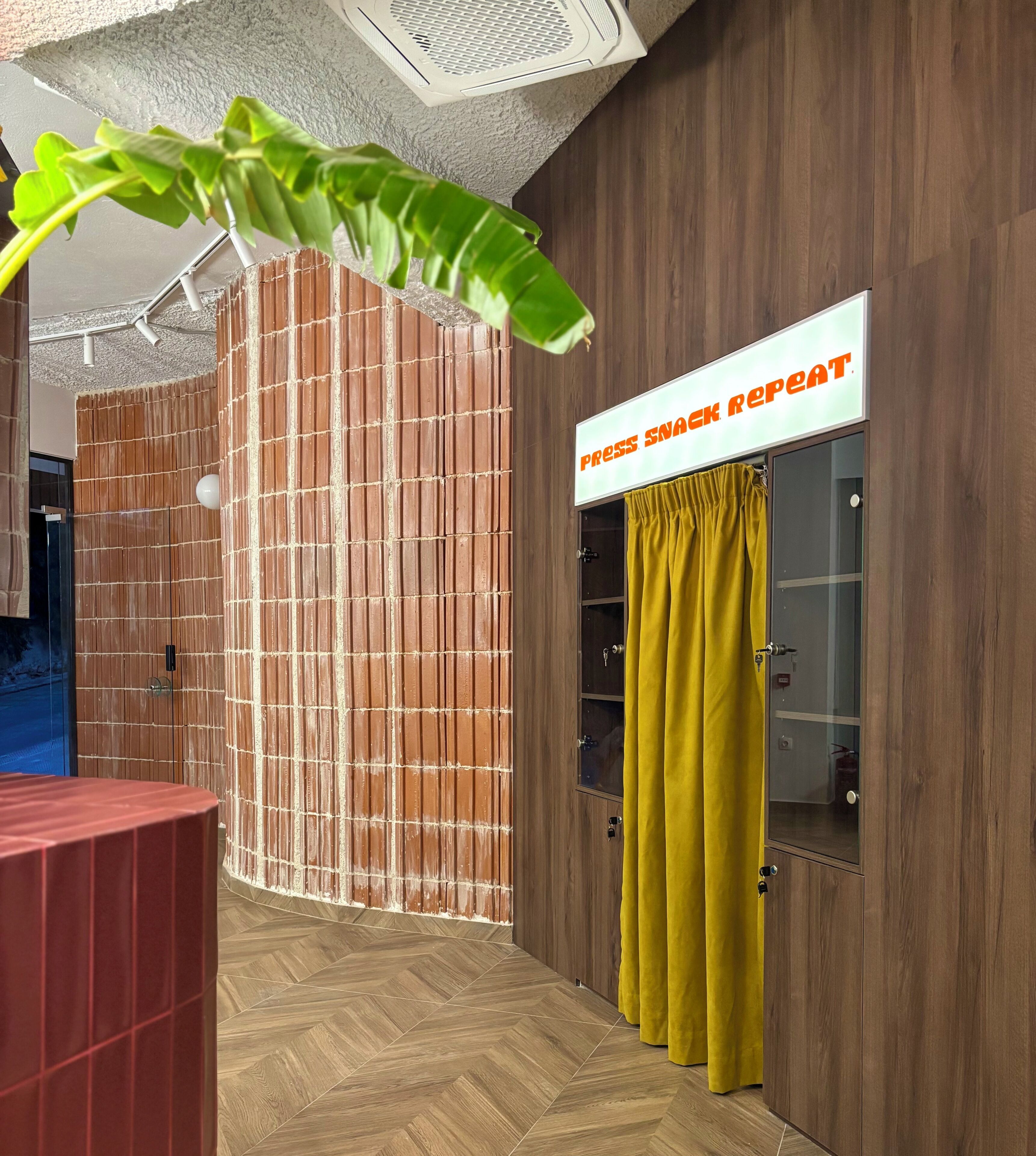 A room with a wooden wall, a yellow curtain, and a sign that reads 'Press Snack Repeat'.