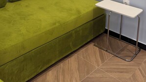 A room with a green sofa, a small white table, and a herringbone-patterned wooden floor.