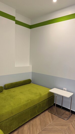 A room with a green sofa, a small white table, and a herringbone-patterned wooden floor.