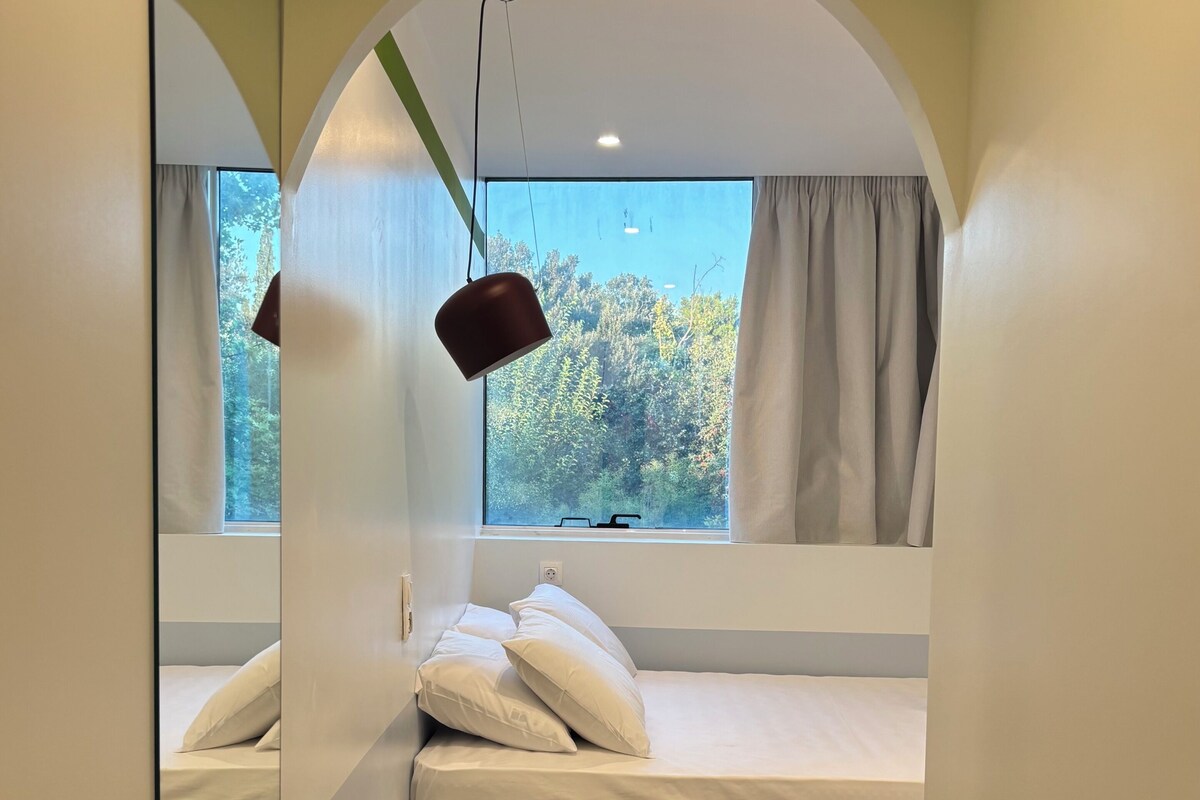 A bedroom with a bed, a hanging lamp, a window with curtains, and a view of trees.