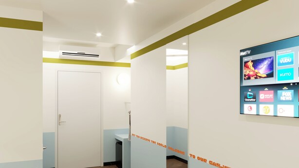 A hallway with a reception desk, a TV screen displaying various channels, and a door.