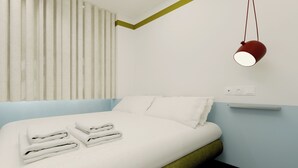 A modern bedroom with a bed, pillows, folded towels, a hanging lamp, and a power outlet on the wall.