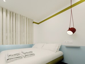 A modern bedroom with a bed, pillows, folded towels, a hanging lamp, and a power outlet on the wall.