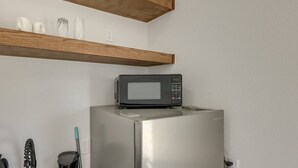 Eine Küche mit einem Edelstahl-Kühlschrank, einer darüberliegenden Mikrowelle, Holzregalen und einigen weißen Keramikgegenständen auf dem Regal.