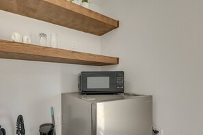 A kitchen with a stainless steel refrigerator, a microwave on top, wooden shelves above, and a few white ceramic items on the shelf. - Studio #3 | Island Time Studio w/Pool, near Beach (South Padre Island)
