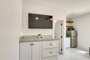 A kitchen with white cabinets, a granite countertop, a flat-screen TV mounted above the counter, a microwave, and a refrigerator. - Studio #3 | Island Time Studio w/Pool, near Beach (South Padre Island)
