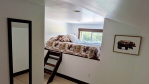 Una camera da letto con un letto, una scala, una finestra e un quadro appeso al muro.