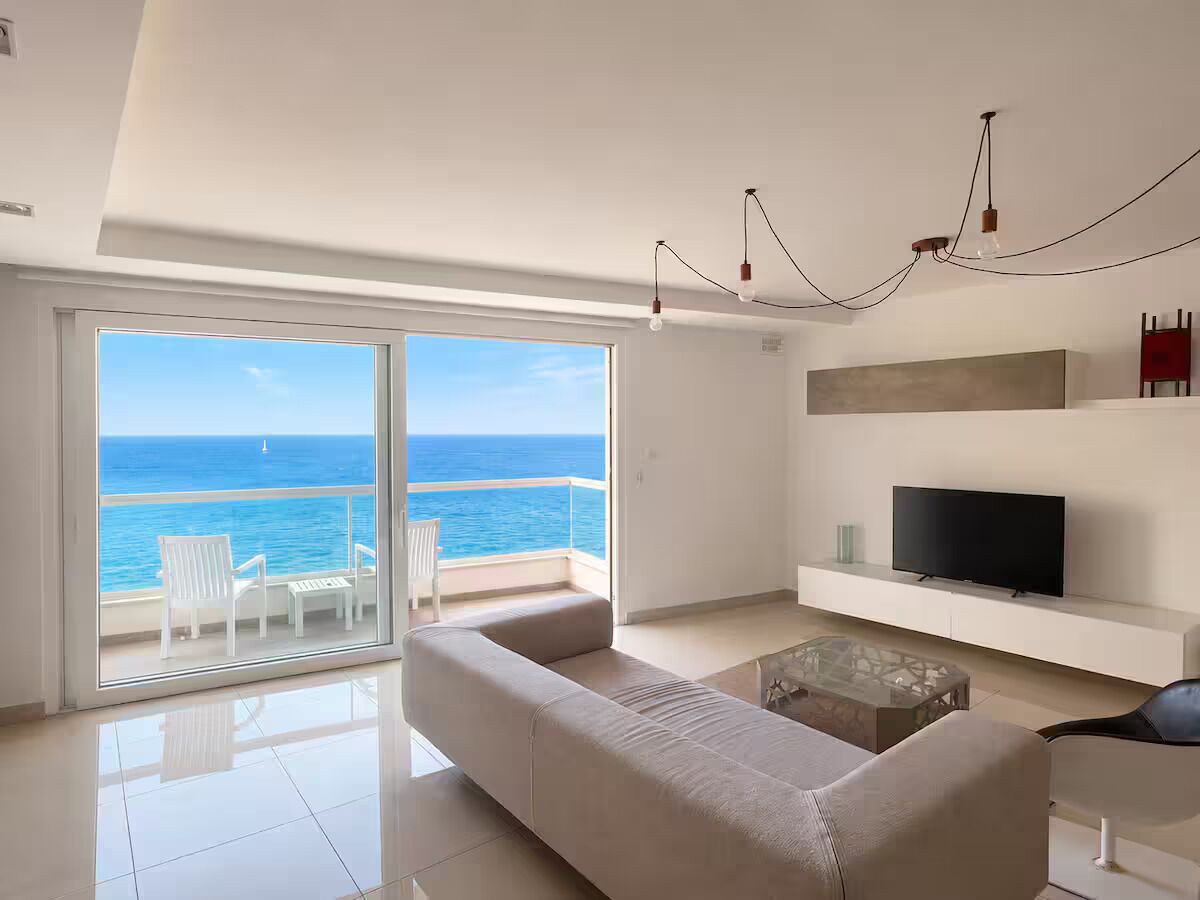 A modern living room with a large sliding glass door leading to a balcony with a view of the ocean.