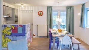 A modern kitchen with white cabinets, a dining area with a table set for four, and a view through the window. - Villa in Hoogerheide With Private Terrace (Hoogerheide)