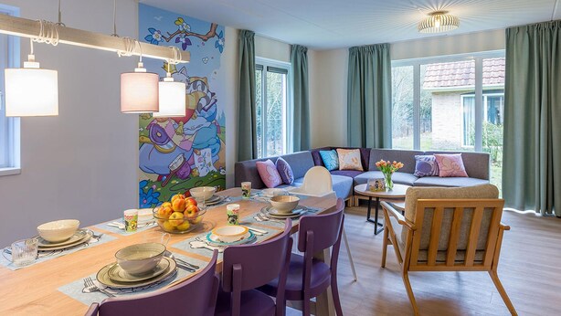 A dining area with a table set for four, a colorful mural on the wall, and a modern sofa in the background. - Villa in Hoogerheide With Private Terrace (Hoogerheide)