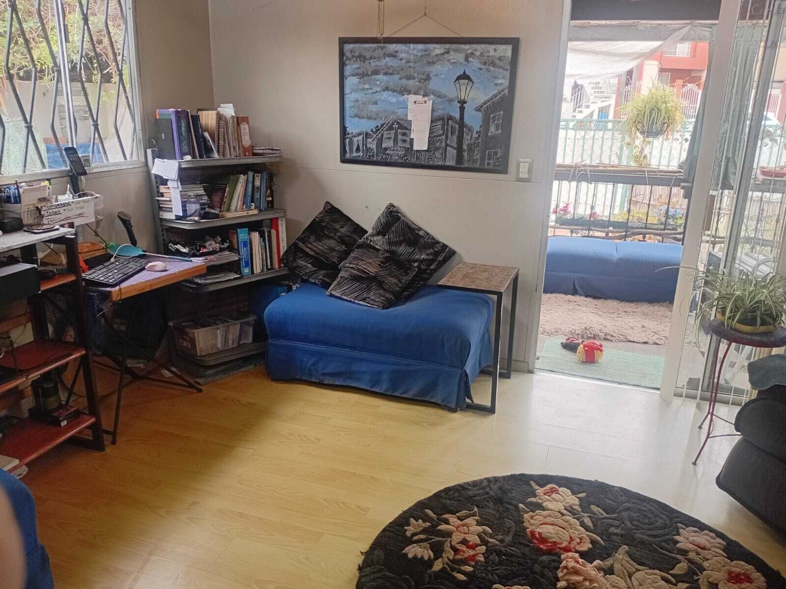 Ein Wohnzimmer mit blauem Sofa, Bücherregal, Schreibtisch mit Computer und einem Gemälde an der Wand.
