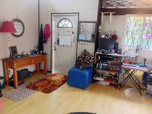 A room with a wooden table, a blue sofa, a computer desk, and a window with a view of trees. - BAJA BEACH FEST Vac. - 7-9th 545. + 1 free 85. massage +20% discount on others. (Playas de Rosarito)