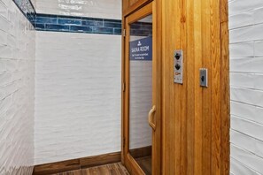 A sauna room with a wooden door, a sign indicating age and height restrictions, and a control panel with buttons and a display.