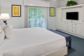 A bedroom with a bed, a TV, a desk, and a window with blinds.