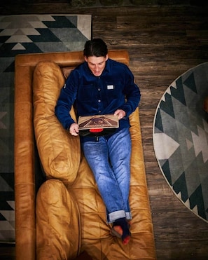 A person lying on a brown leather couch with a patterned rug in the background.