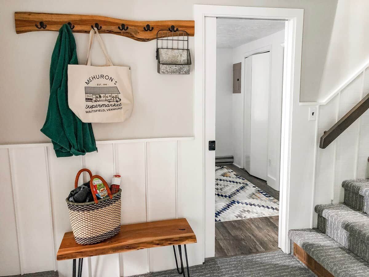 A hallway with a bench, a hanging tote bag, and a basket with items.