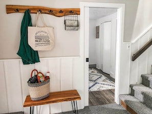 A hallway with a bench, a hanging tote bag, and a basket with items.